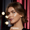 Eine Frau trägt den Mesauda Beauty Nude Venus Puder und blickt in die Kamera, hinter ihr sind drei Leuchtpunkte. Unten steht: PRIMA