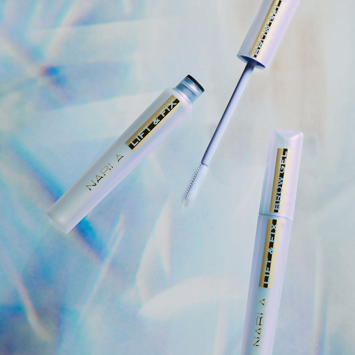 Zwei Lift & Fix Brow Gel-Tuben, eine davon mit herausgezogenem Applikator, werden vor einem abstrakten Hintergrund in Hellblau präsentiert.