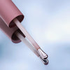 Nahaufnahme eines rosafarbenen Applikators des Wide Awake Full Coverage Concealer mit silberner Spitze vor hellem Hintergrund, gespiegelt auf glatter Oberfläche.