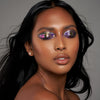 Person mit geschlossenen Augen und mittel-braunem Hautton präsentiert schimmernden, irisierenden Make-up-Look mit den Infinite Chrome Flakes Superstar.