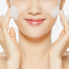 Eine Frau lächelt, während sie im Rahmen ihrer Hautpflegeroutine den Low-pH Good Morning Gel Cleanser aufträgt.