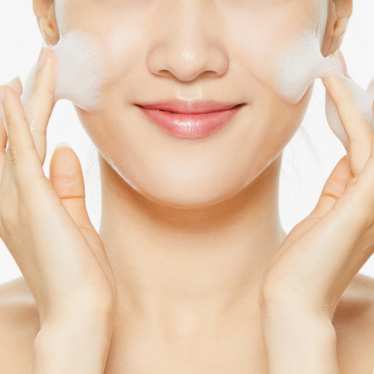 Eine Frau lächelt, während sie im Rahmen ihrer Hautpflegeroutine den Low-pH Good Morning Gel Cleanser aufträgt.