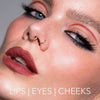 Nahaufnahme einer Frau mit auffälligem Make-up, Lidstrich und roten Lippen, kreiert mit dem Crayon Lipliner Cherry von LH Cosmetics. Text: Lips | Eyes | Cheeks.
