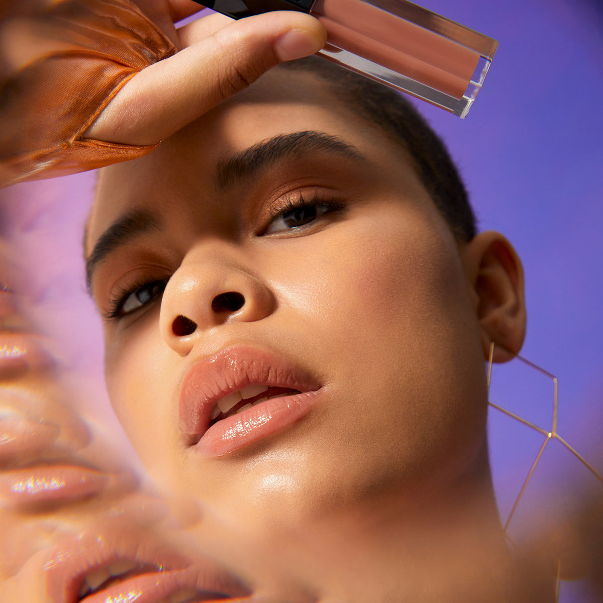 Eine Frau präsentiert den Gloss Matrix Lipgloss von Mesauda Beauty und trägt einen goldenen, rechteckigen Ohrring.