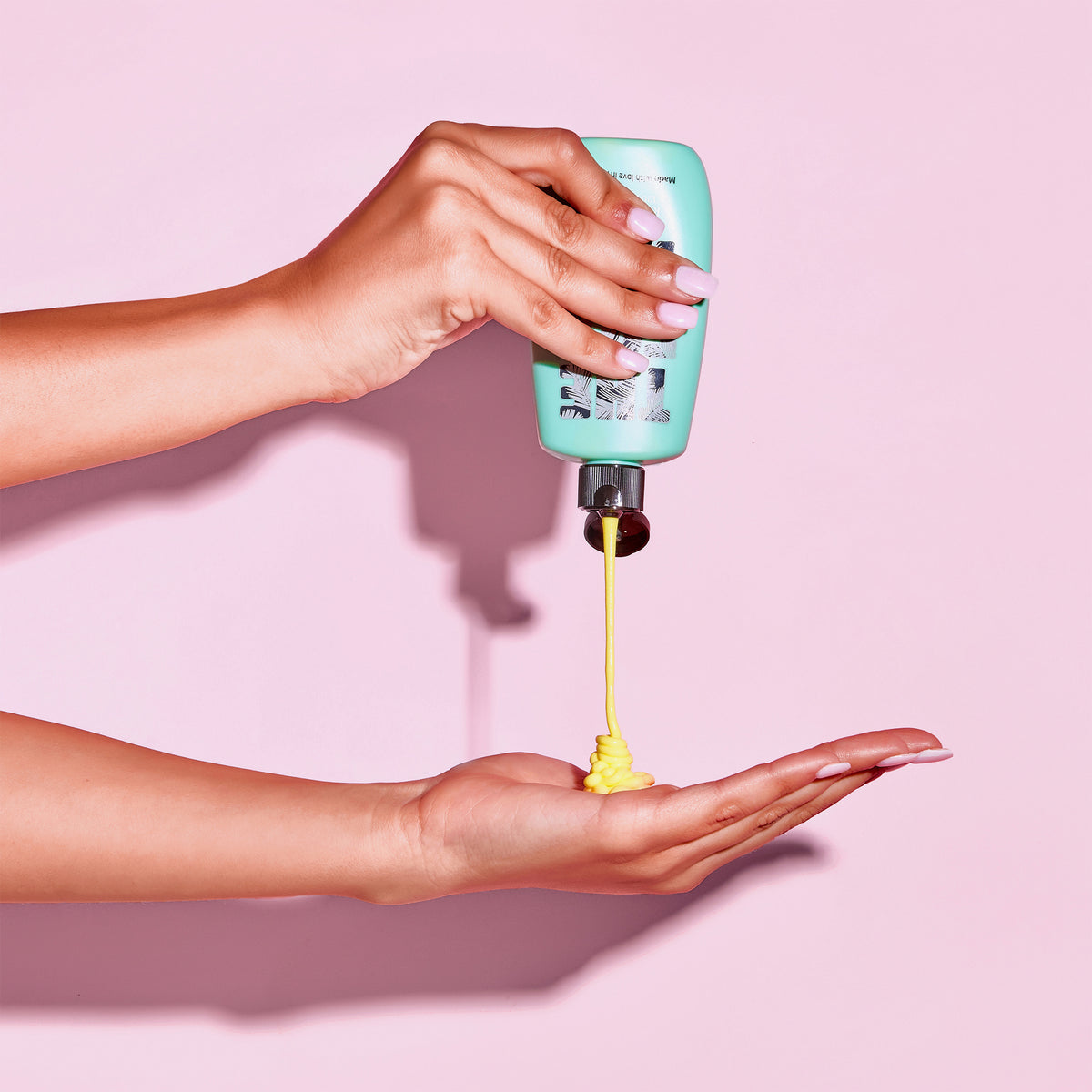 Rapid Tanning Elixir aus einer grünen Flasche wird auf eine Hand vor rosa Hintergrund gegeben.