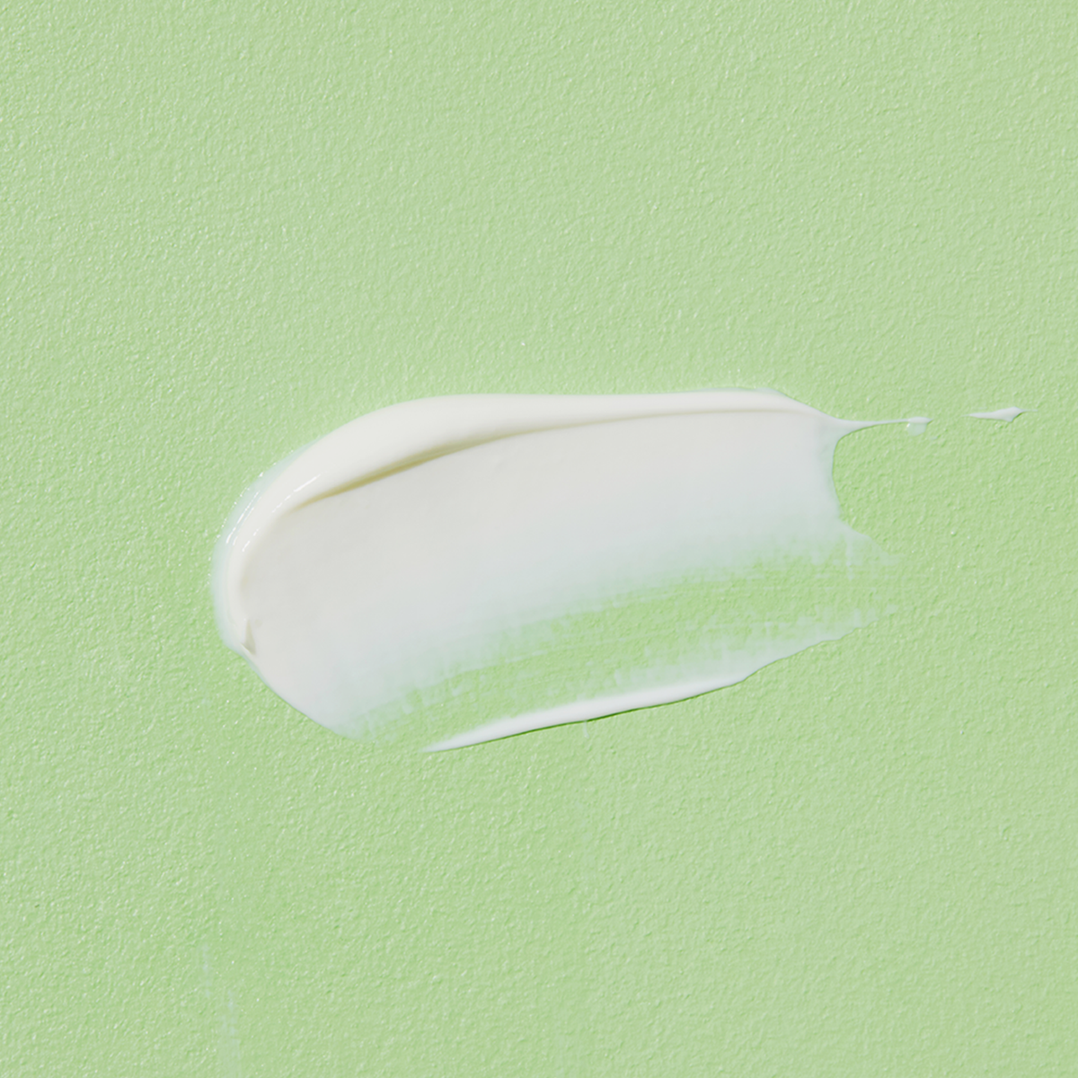 Ein cremig weißer Swatch der Aloe Soothing Sun Cream SPF50+ PA+++ auf einer hellgrünen strukturierten Oberfläche.