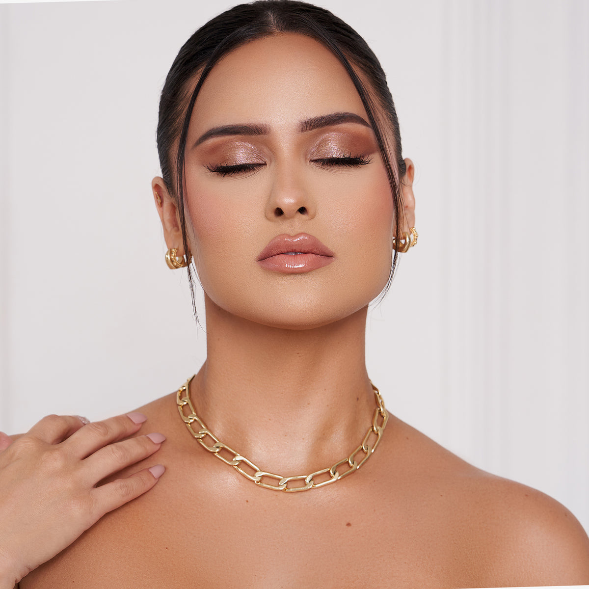 Frau mit geschlossenen Augen, Goldschmuck und zurückgekämmtem Haar, präsentiert vor hellem Hintergrund ein Nude-Make-up, das mit der Essential Palette kreiert wurde.