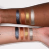 Zwei Arme unterschiedlicher Hautfarbe zeigen vier metallische Lidschattenmuster der LH Cosmetics Basic Elements in Blau, Kupfer, Gold und Silber.
