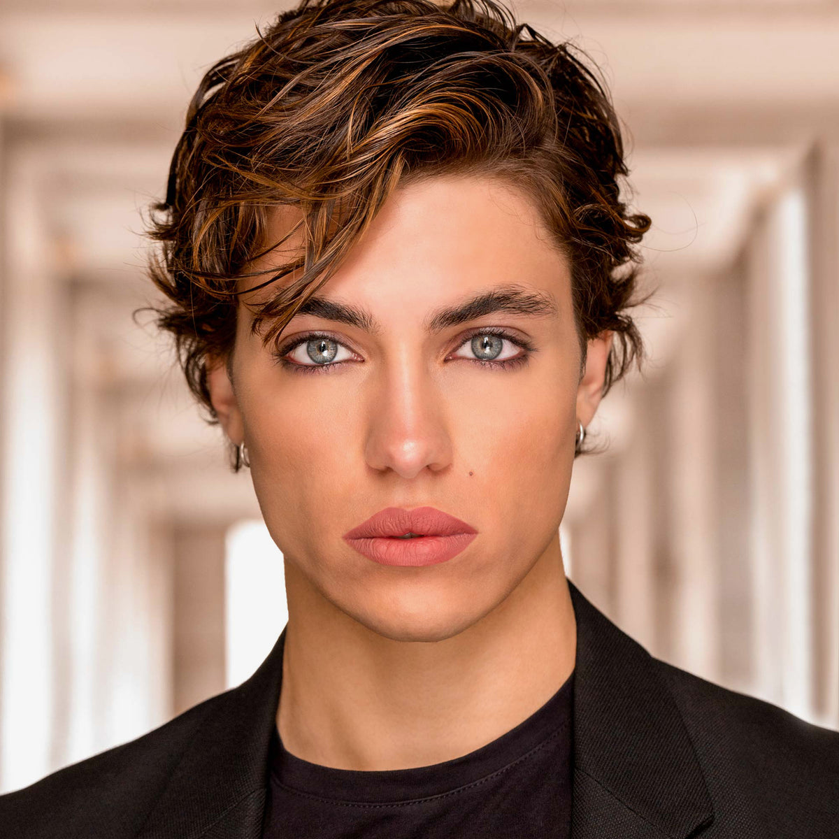 Junge Person mit braunem Haar und trägt den Cult Matte Lipstick von Mesauda Beauty und eine schwarze Jacke.