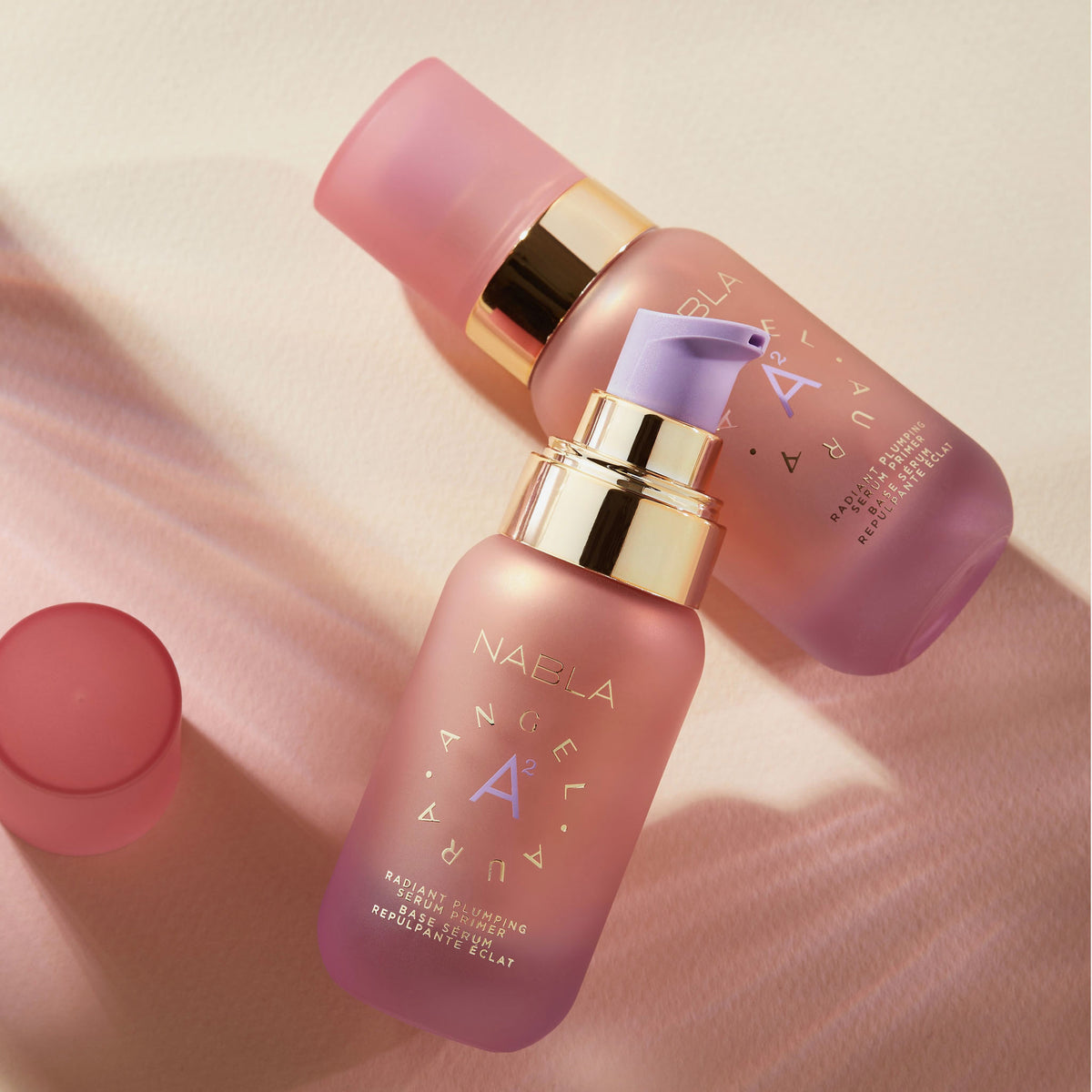 Zwei rosa mattierte Flaschen Angel Aura-Serum mit goldenen Akzenten werden auf einem zartrosa Hintergrund präsentiert.