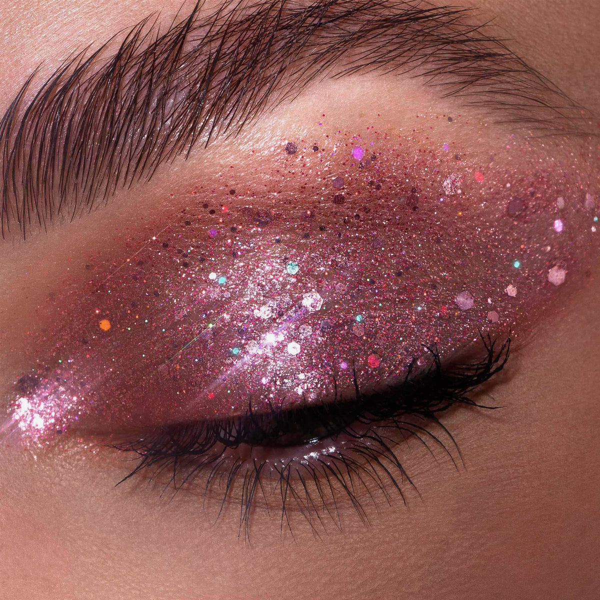 Ein geschlossenes Auge zeichnet sich durch lange, dunkle Wimpern und rosa Schimmer aus der Glorious Lights Glitter Palette aus.
