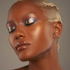 Person mit geschlossenen Augen und dunklem Hautton präsentiert schimmernden, irisierenden Make-up-Look mit den Infinite Chrome Flakes Pixie Dust.