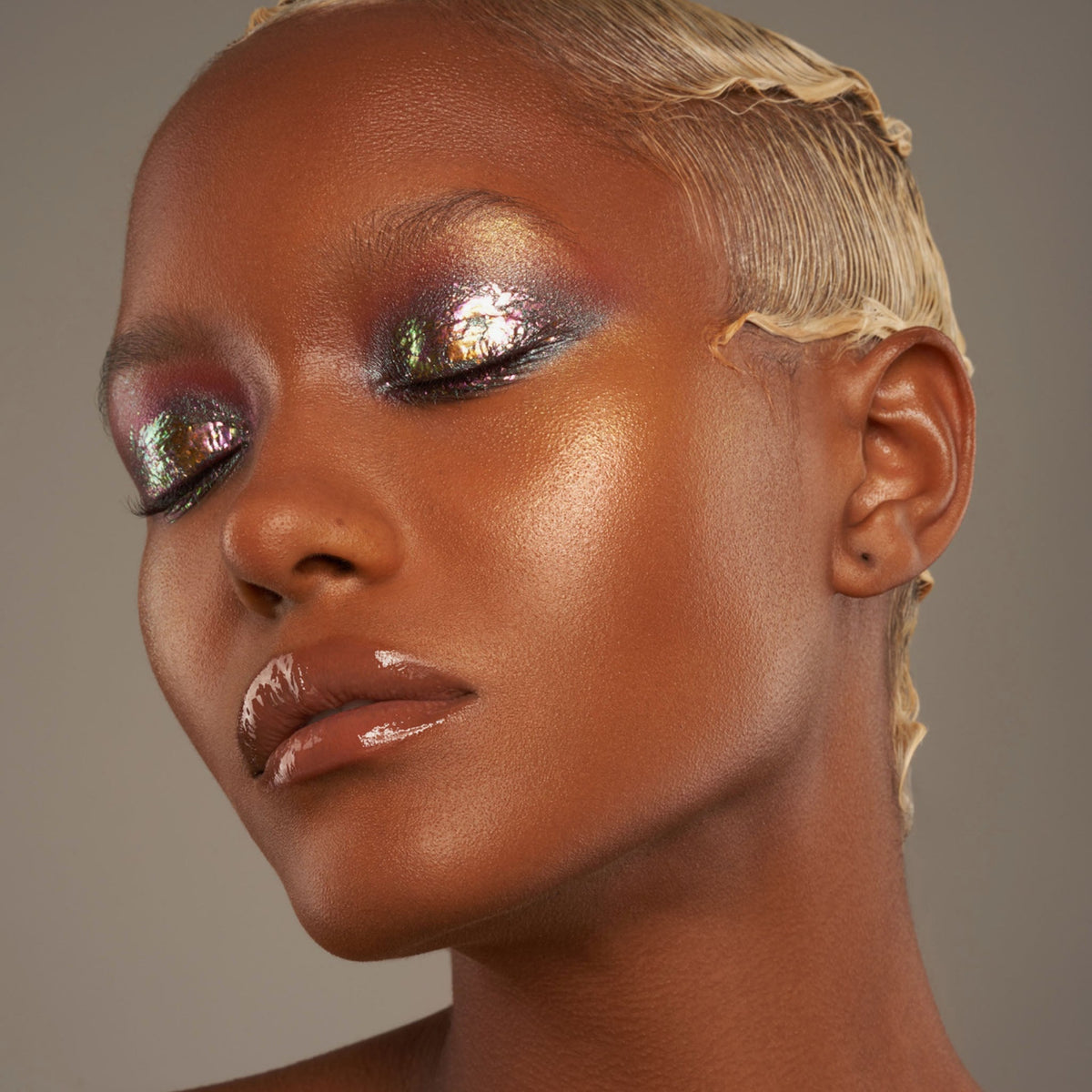Person mit geschlossenen Augen und dunklem Hautton präsentiert schimmernden, irisierenden Make-up-Look mit den Infinite Chrome Flakes Pixie Dust.