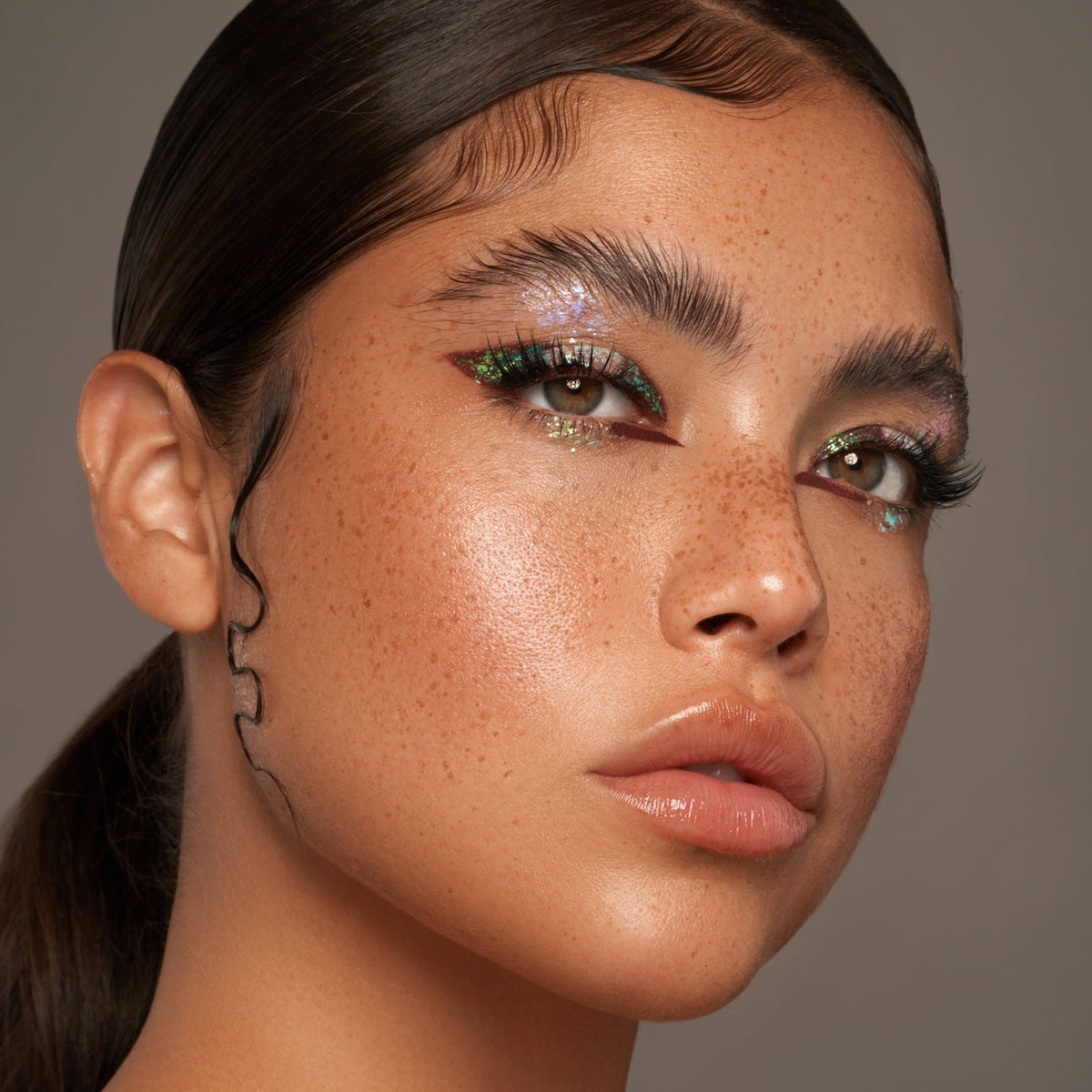 Person mit geschlossenen Augen und mittlerem Hautton präsentiert schimmernden, irisierenden Make-up-Look mit den Infinite Chrome Flakes.