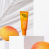 Eine Tube Bondi Sands Lip Balm SPF 50+ in Orange steht auf einem weißen Sockel, umgeben von Mangos 
