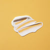 Cremig weißer Swatch der SPF50+ Lotion Fragrance Free  auf einem glatten, gelben Hintergrund.