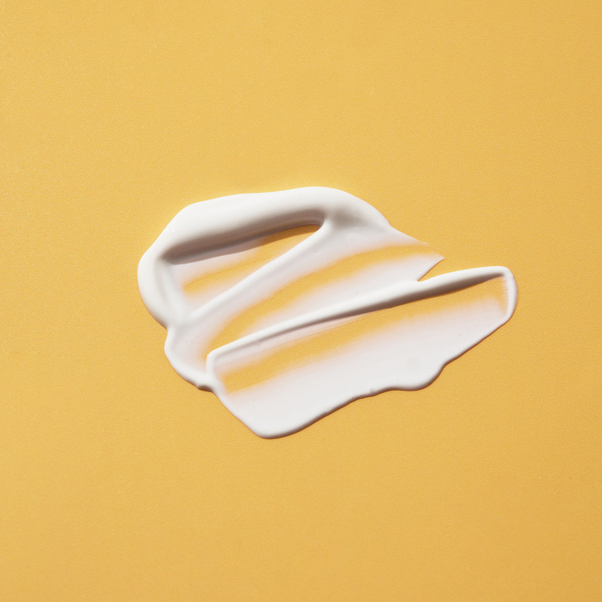 Cremig weißer Swatch der SPF50+ Lotion Fragrance Free  auf einem glatten, gelben Hintergrund.
