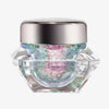Transparenter Tiegel Infinite Chrome Flakes Pixie Dust mit lila-blau schillerndem Inhalt und silbernem Deckel vor weißem Hintergrund.