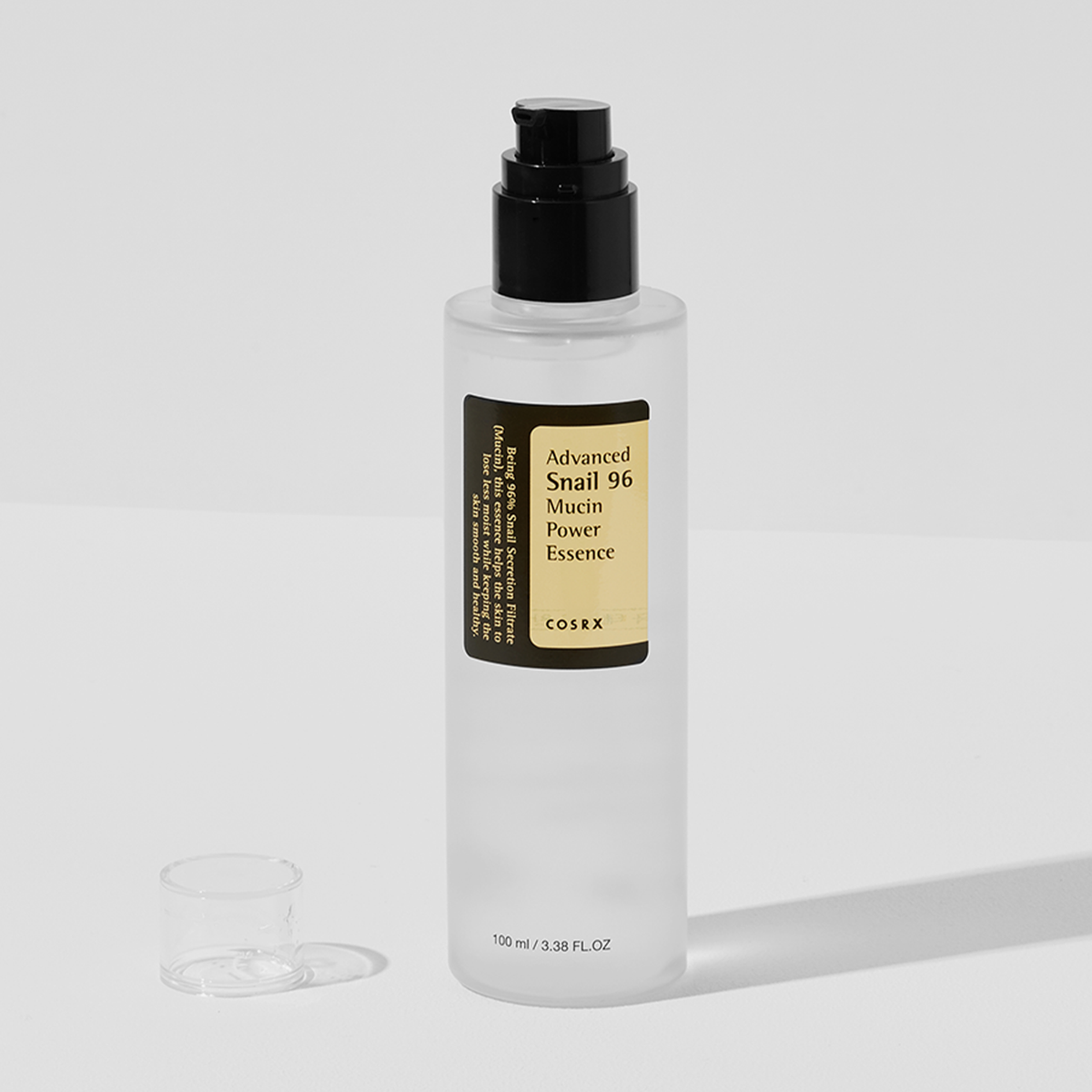 Eine durchsichtige Flasche COSRX Advanced Snail 96 Mucin Power Essence mit schwarzem Pumpspender auf einer weißen Oberfläche.