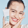 Eine lächelnde Frau mit strahlender Haut hält eine Tube der Ultimate Nourishing Rice Overnight Spa Mask.