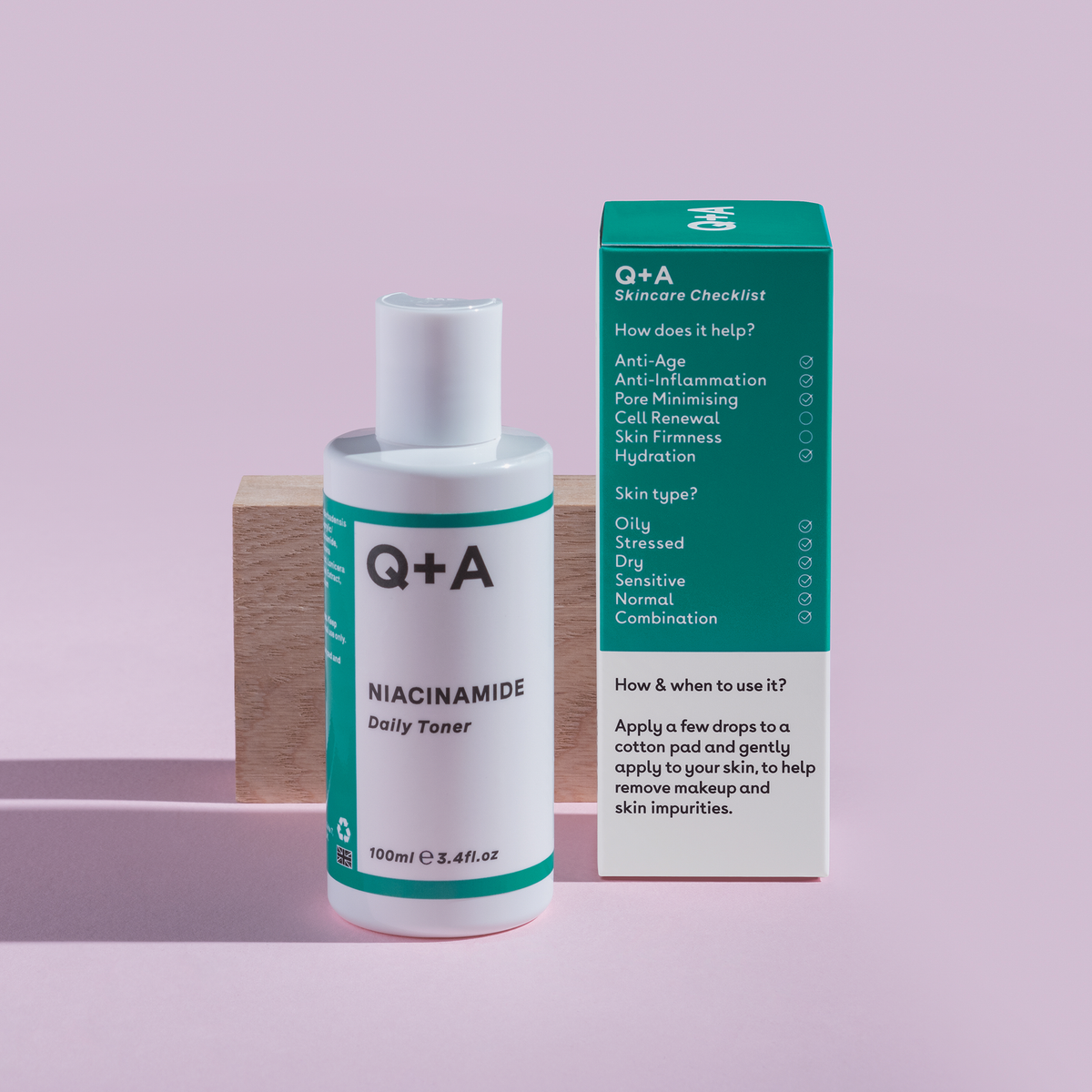 Niacinamide Daily Toner und Schachtel auf rosa Hintergrund vor einem Holzblock präsentiert.